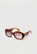 Sonnenbrille aus Schildpatt mit ovalen Rahmen, verlaufsfähigen Gläsern und goldenen Hardware-Details an den Schläfen. Glatte, glänzende Kunststoffoberfläche.