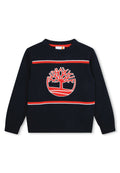 Marineblaue gestrickte Pullover mit einem großen roten und weißen Baum-Logo, horizontalen roten und weißen Streifen sowie einem gerippten Rundhalsausschnitt und Bündchen.