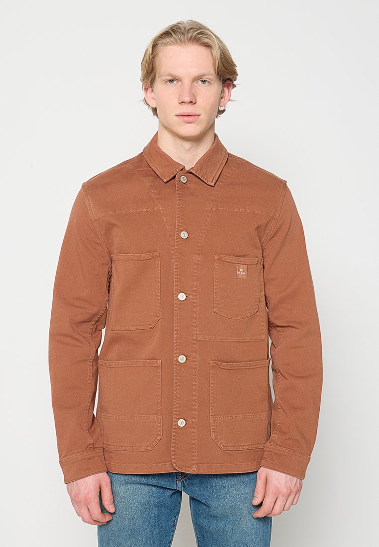 Braune Canvas-Jacke mit Knopfleiste, vier Taschen und Kragen. Verfügt über eine einfarbige Textur und ein schlichtes Design. Wird mit blauen Jeans getragen.