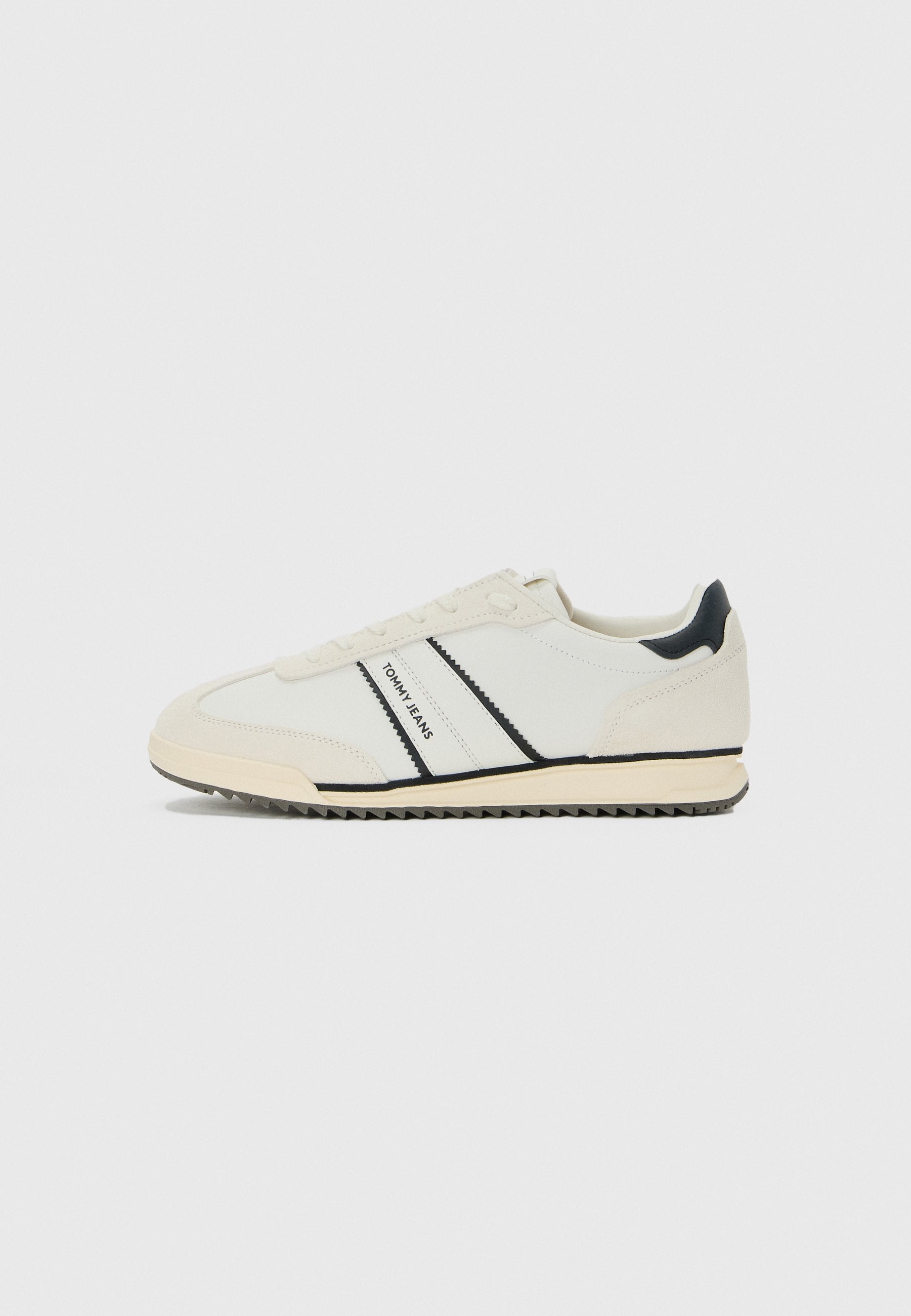 Weiße lässige Sneaker mit schwarzen Akzenten und "TOMMY JEANS"-Branding an der Seite, flache Sohle mit gerilltem Boden und Schnürdesign.