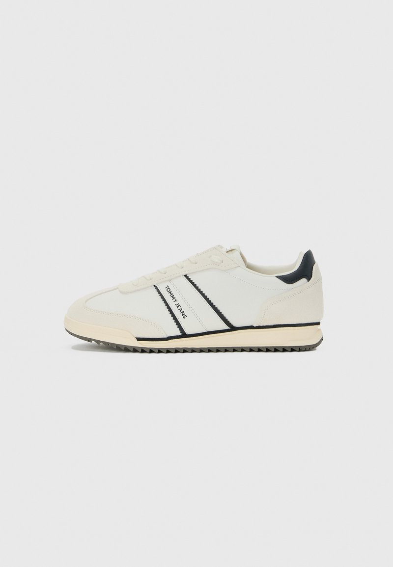 Weiße lässige Sneaker mit schwarzen Akzenten und "TOMMY JEANS"-Branding an der Seite, flache Sohle mit gerilltem Boden und Schnürdesign.