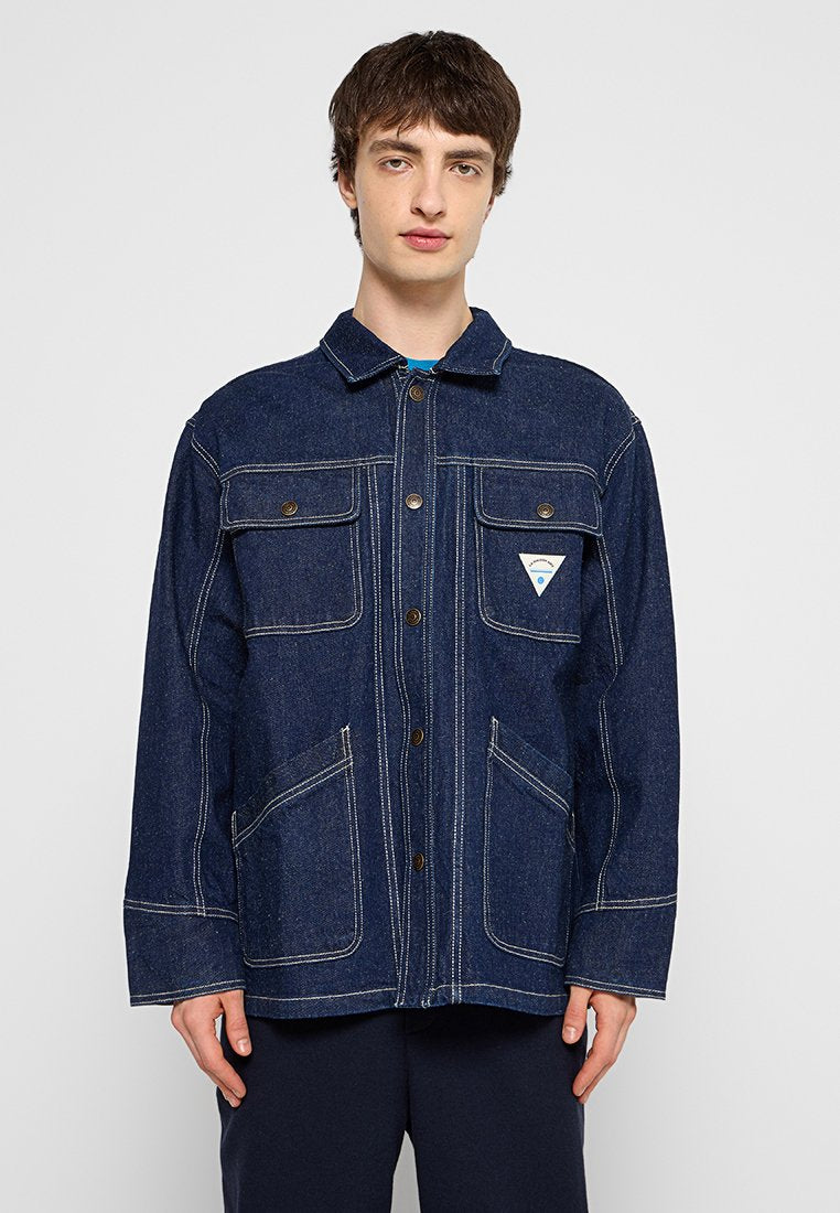 Dunkelblaue Jeansjacke mit zwei Brusttaschen, ausgeprägter Naht und einem dreieckigen Logo-Patch auf der linken Tasche.