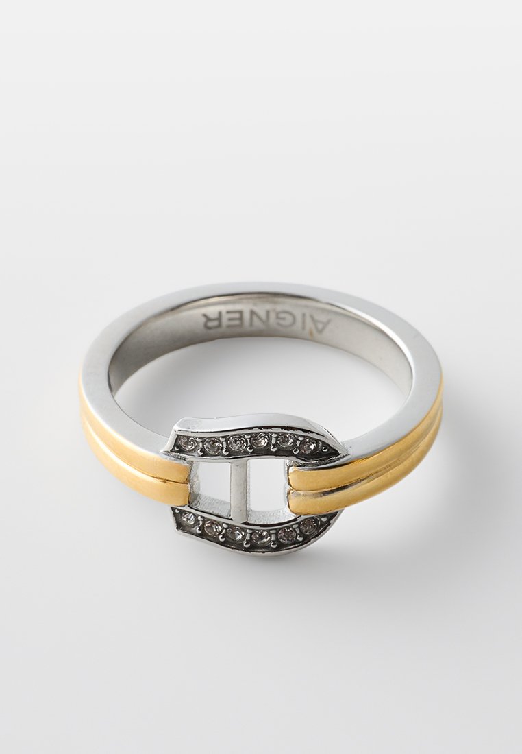 Silber- und Goldring mit einem mittleren Schnallenelement, das mit kleinen, klaren Edelsteinen verziert ist, und dem eingravierten Markennamen "AIGNER" auf der Innenseite des Rings.