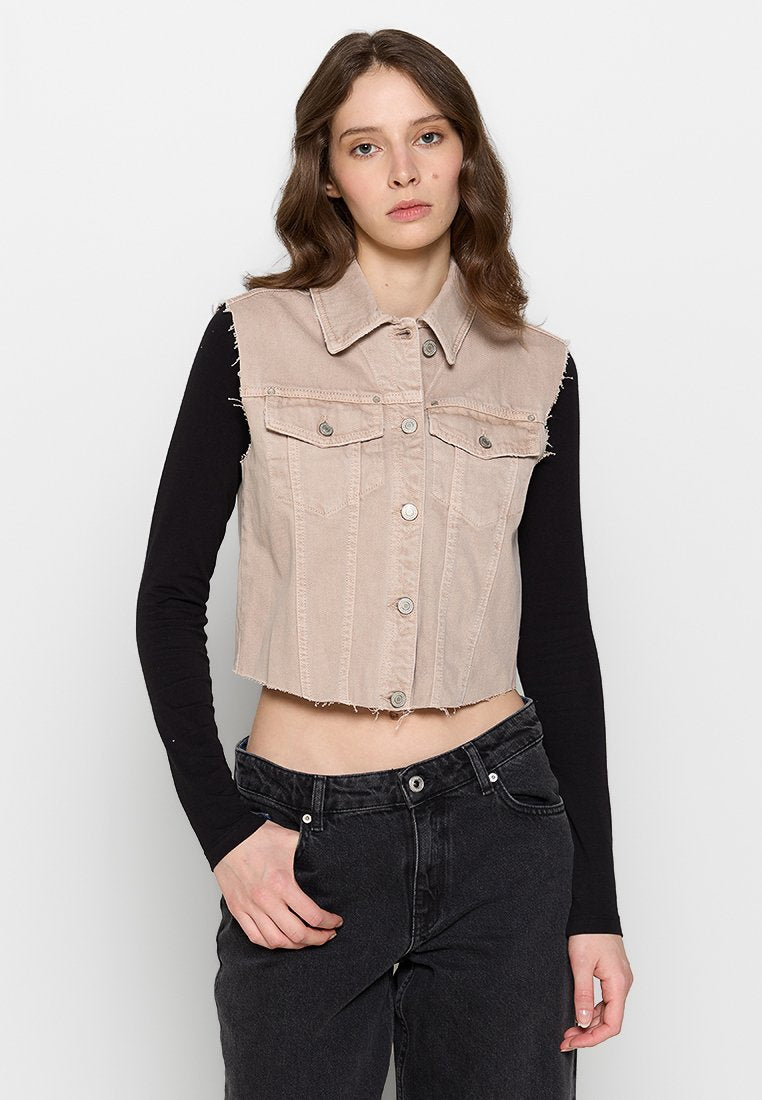 Helle beiger, cropped Denim-Weste mit kragenförmigem Ausschnitt, Knopfleiste und Brusttaschen. Über einem schwarzen Langarmshirt getragen.
