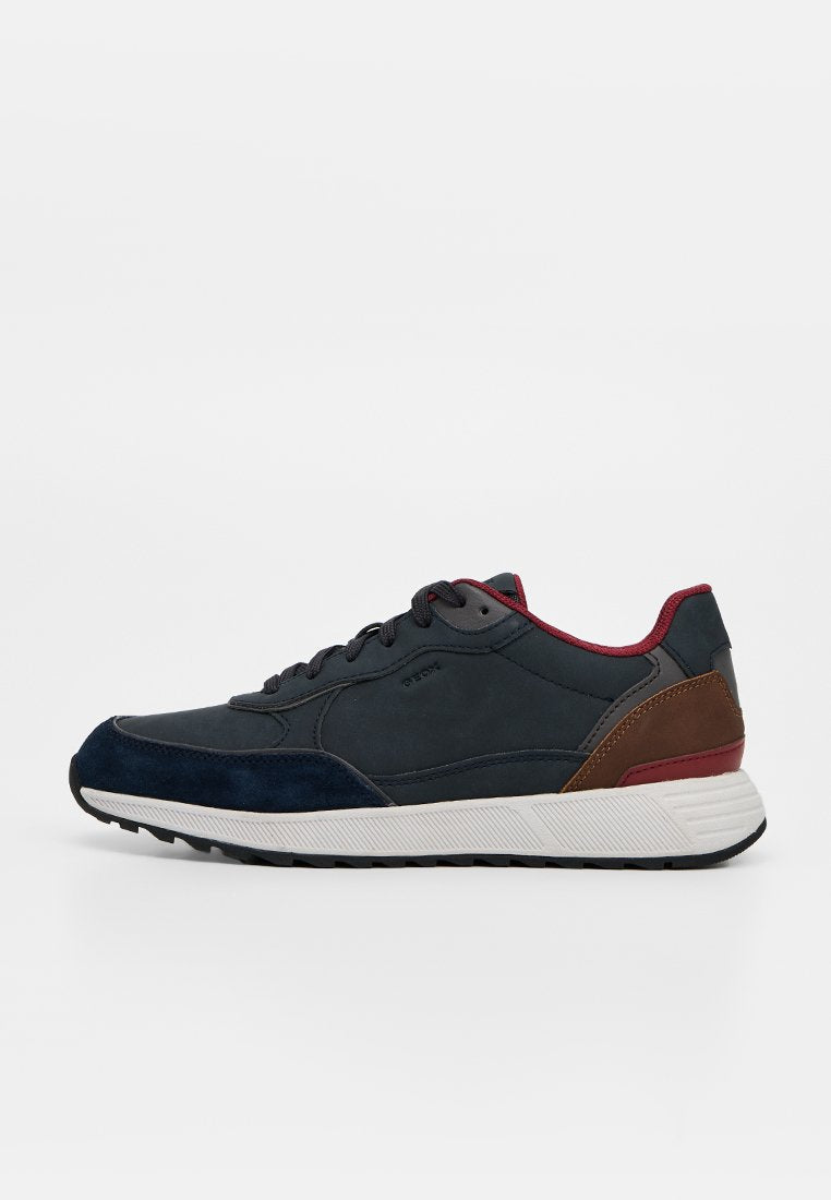 Dunkelblauer und brauner Sneaker mit weißer Sohle, schwarzen Schnürsenkeln und rotem Innenfutter, von der Seite auf weißem Hintergrund gezeigt.