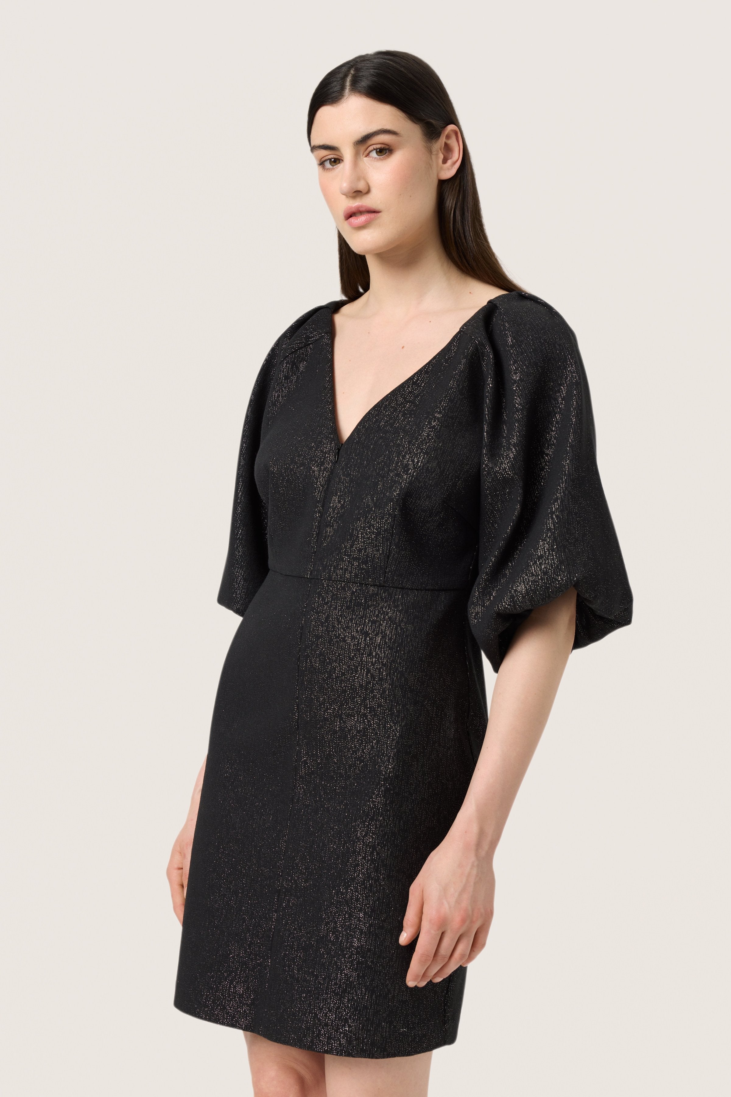 Schwarzes Kleid mit V-Ausschnitt, Puffärmeln und taillierter Silhouette. Der Stoff hat einen strukturierten Glanz mit dezenten metallischen Akzenten.