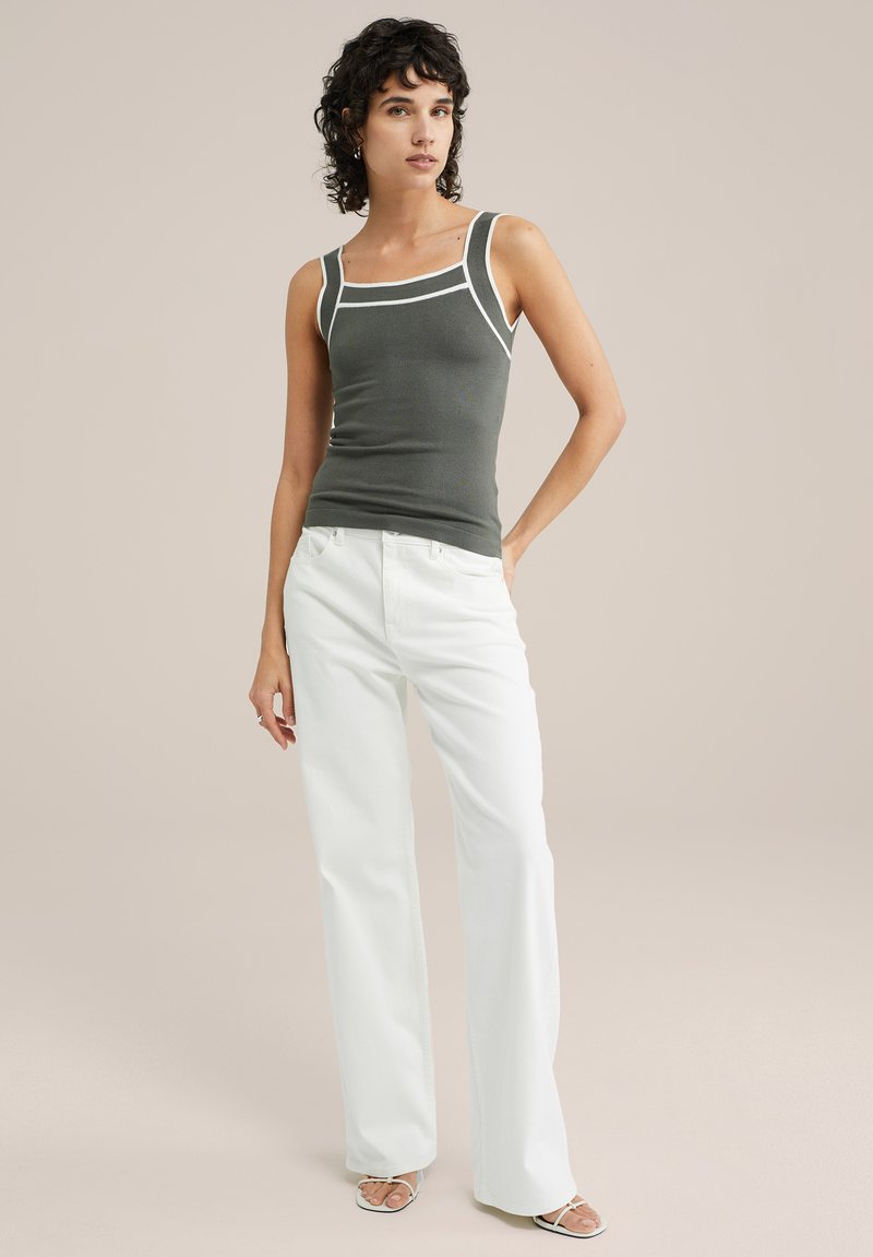 Graues, tailliertes Tanktop mit weißer Kante, kombiniert mit weißen Schlagjeans. Das Modell steht vor einem neutralen Hintergrund. Glatte Textur und modernes Design.