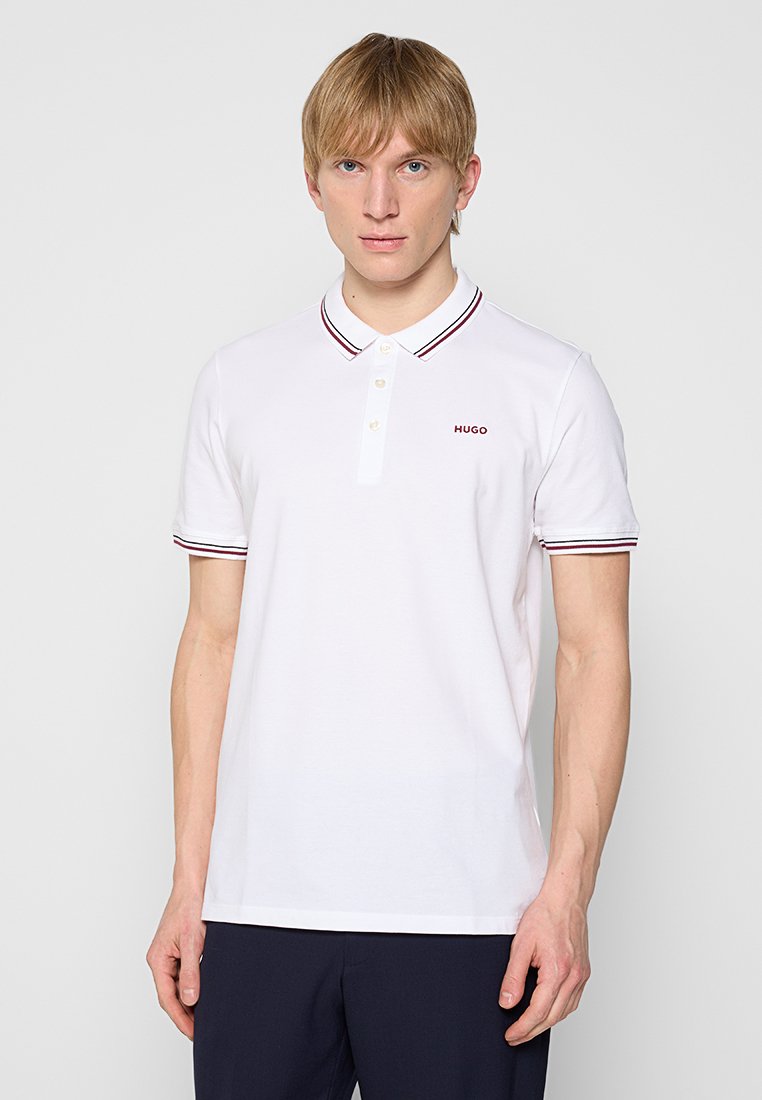Weißes Polohemd mit einer Zwei-Knopf-Leiste, einem rot und navyblau gestreiften Kragen und kleinem roten "HUGO"-Logo auf der Brust. Aus weichem Baumwollstoff.