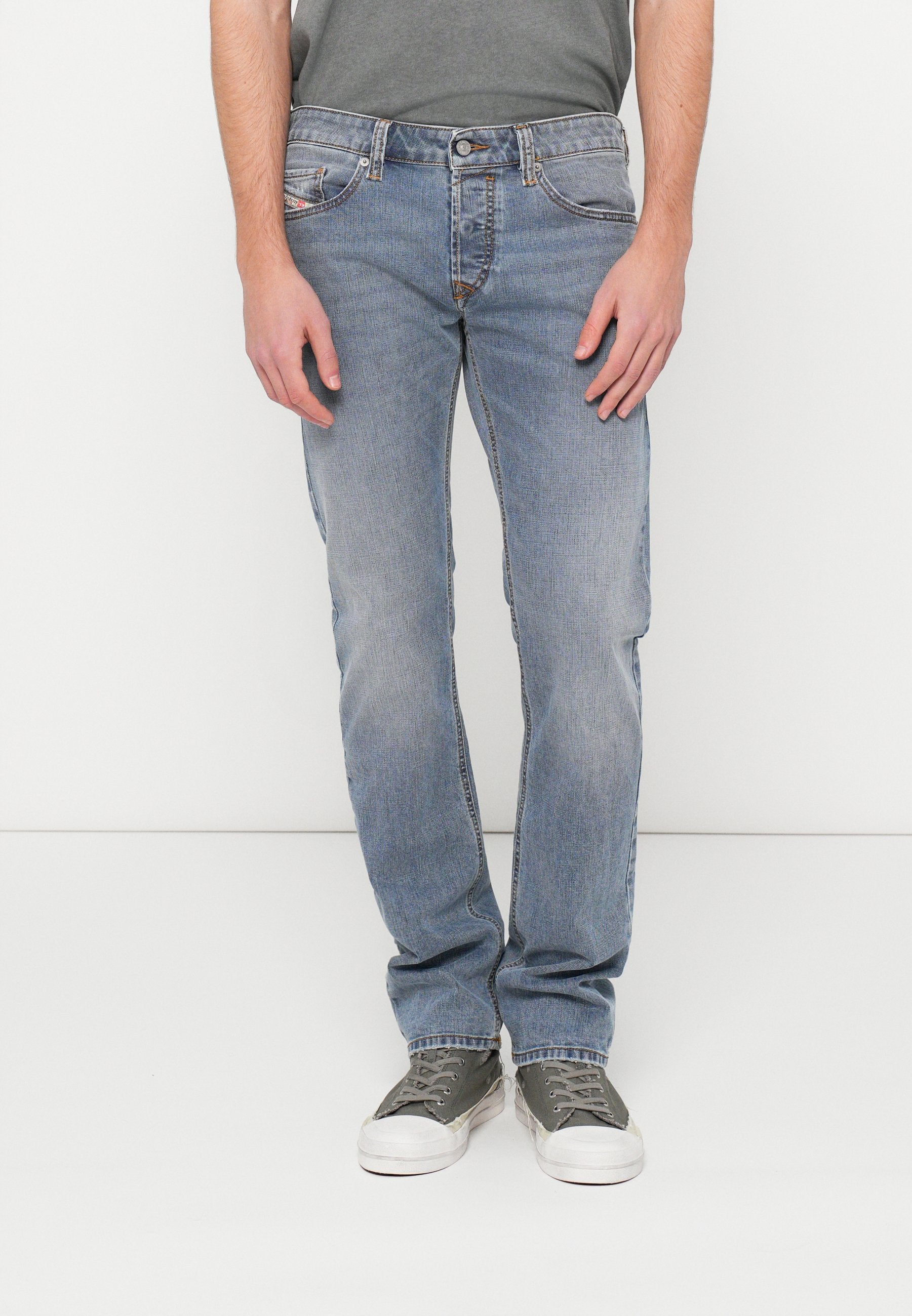 Hellblaue Denim-Jeans mit geradem Schnitt, ausgestattet mit einem klassischen Fünf-Taschen-Design und dezenten Steppnähten. Kombiniert mit grauen Turnschuhen.