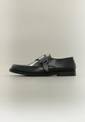 Schwarzer Lederschuh mit seitlicher Schnalle und Nahtdetail, im Profil vor neutralem Hintergrund gezeigt.
