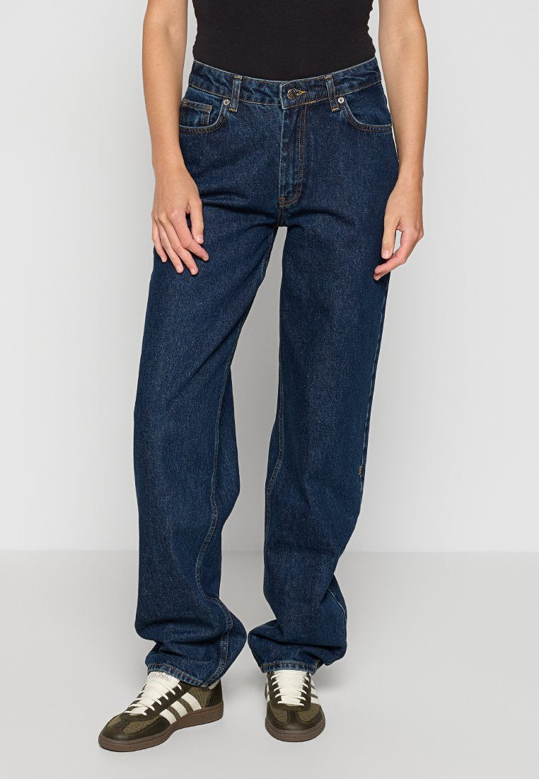 Dunkelblaue Jeans aus Denim mit lockerer Passform, ausgestattet mit Vorder- und Hintertaschen, Gürtelschlaufen und kontrastierenden Nähten. Kombiniert mit dunklen Schuhen.