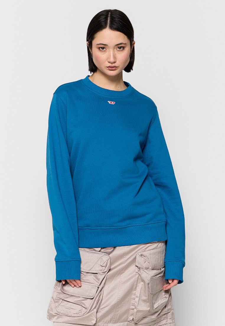 Türkiser Baumwollpullover mit gerippter Textur, Rundhalsausschnitt, langen Ärmeln und einem kleinen roten Logo auf der Brust, kombiniert mit einem beigen Cargo-Rock.