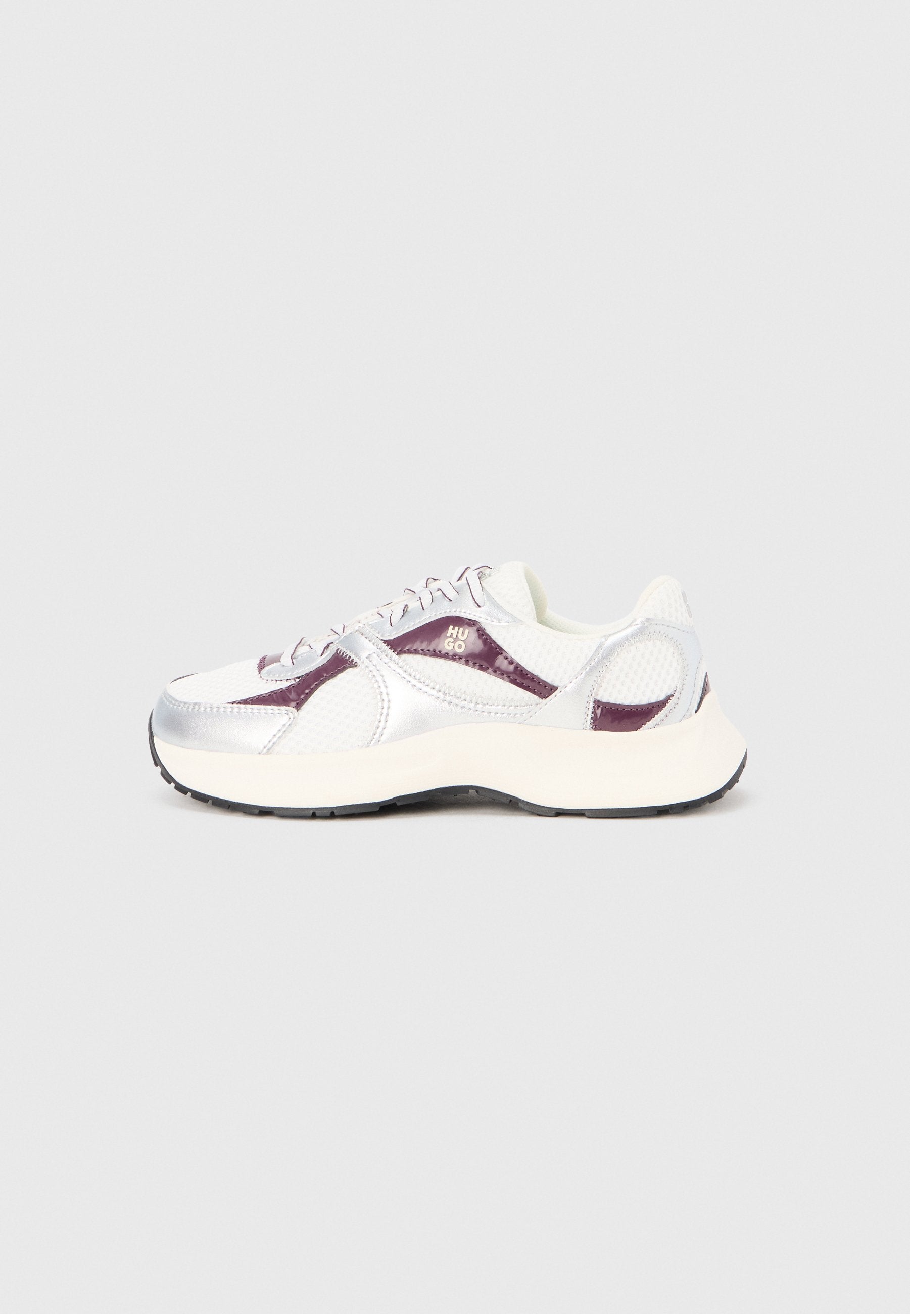 Weißer und silberner Sportschuh mit Mesh- und Lackleder-Akzenten, versehen mit lilafarbenen Details, einer gepolsterten Sohle und abgerundetem Design.