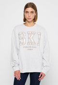 Grauer Sweatshirt mit langen Ärmeln, das in der Mitte das Wort "SKI" in fettem Karomuster und "COLORADO 1989" in braunem Text zeigt. Weiches Material.