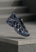 Salomon Trailrunning-Schuh mit einem Obermaterial aus Mesh in Marineblau und Grau, einem Schnellschnürverschluss und einer strukturierten Gummisohle.
