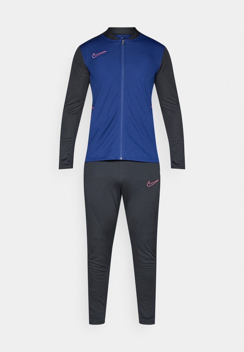 Männlicher Sportanzug mit blauer Jacke mit Reißverschluss und schwarzen Ärmeln sowie Hose, die pinkfarbene Nike-Logos auf der Brust und dem Oberschenkel trägt.