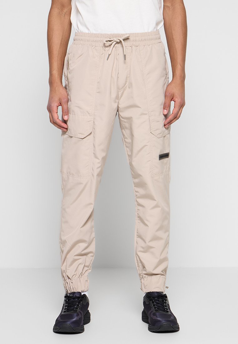 Beige Cargo-Hosen mit elastischem Bund, Kordelzug, Seitentaschen und elastischen Bündchen. Hergestellt aus leichtem, glattem Stoff.