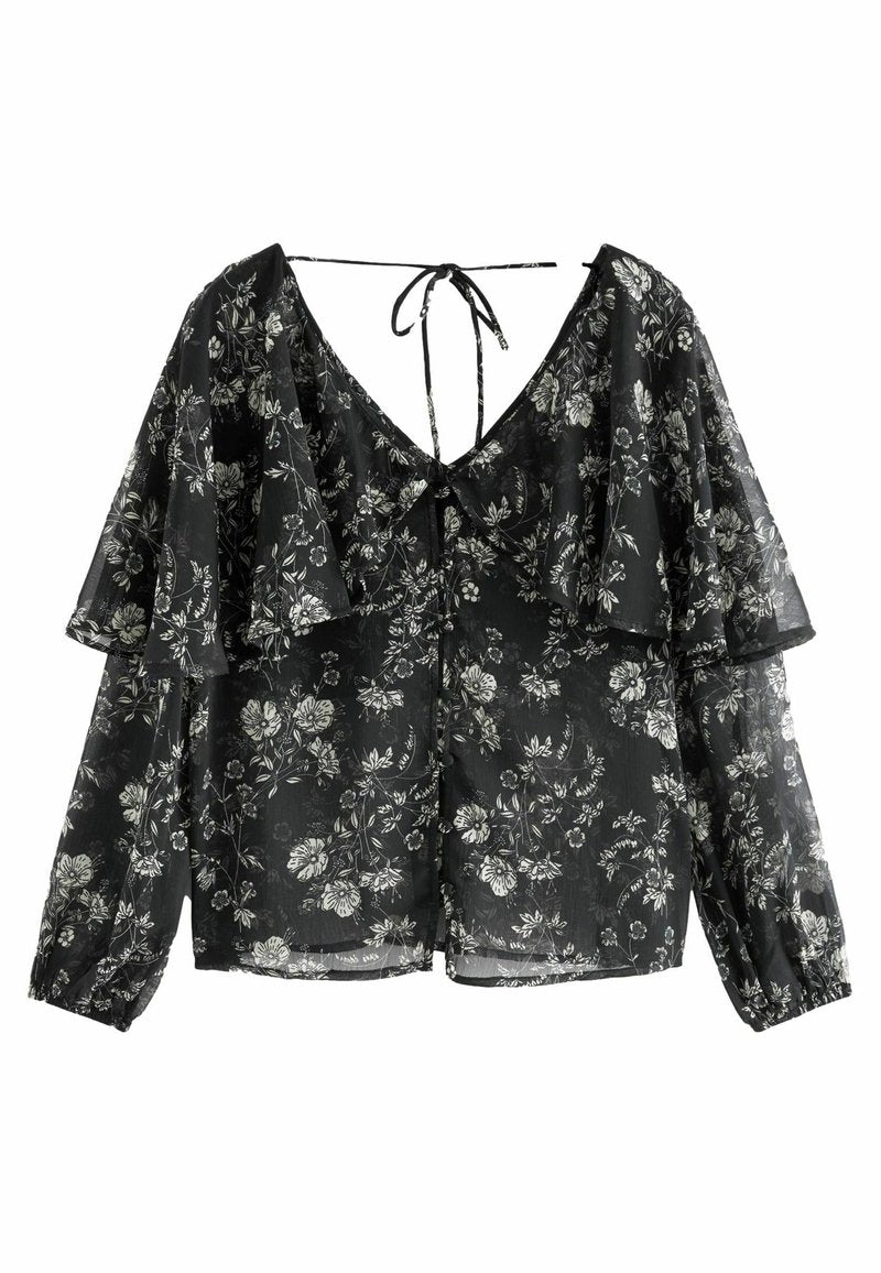 Schwarze Bluse mit floralem Muster, V-Ausschnitt, Rüscheln an den Ärmeln und einer Schleife im Rücken. Hat weiße Blumenmuster auf dem durchscheinenden Stoff.