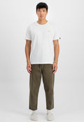 Weißes Baumwoll-T-Shirt mit Rundhalsausschnitt und kleinem goldenen Logodetail, kombiniert mit olivgrünen Hosen und hellgrauen Slippern.