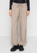 Beige weit geschnittene Hose mit vorderen Falten und Kordelzugbund, kombiniert mit schwarzen schnürbaren Plateauschuhen und einem schwarzen Langarmtop.