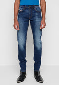 Dunkelblaue Jeans im Slim-Fit-Stil mit ausgebleichten Stellen, gestickten Akzenten und einem Fünf-Taschen-Design. Kombiniert mit schwarzen Knöchelstiefeln.