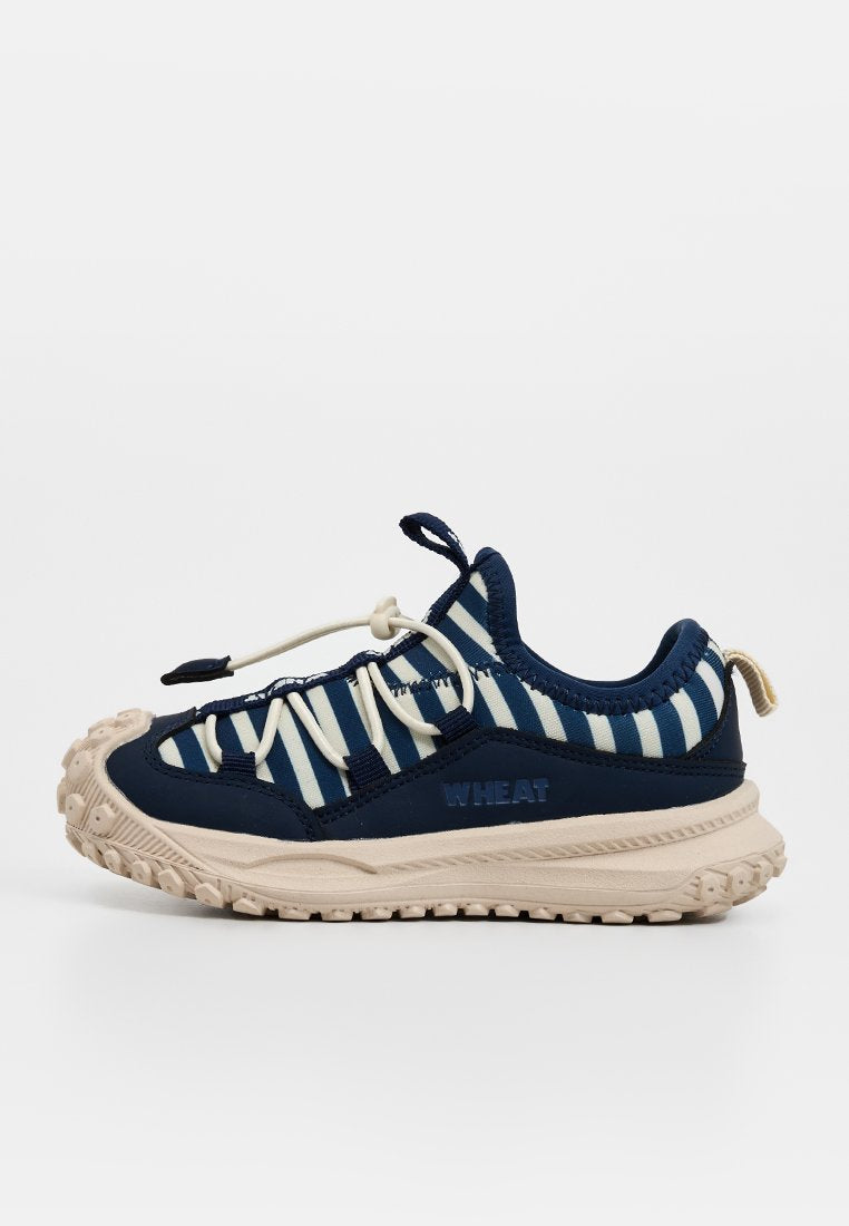 Marineblaue und weiße gestreifte Sneaker mit beiger Sohle, elastischen Schnürsenkeln und robustem Profil, seitlich mit "WHEAT" gebrandet.