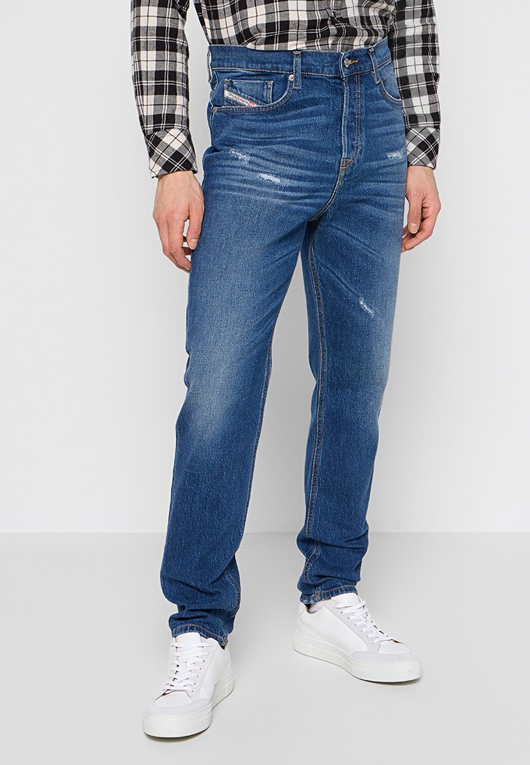 Blaue Denim-Jeans mit geradem Bein, ausgewaschenem Frontbereich und klassischem fünf-taschen Design, kombiniert mit weißen Sneakers und einem schwarz-weißen karierten Hemd.