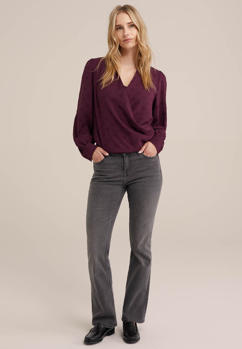 Lila Bluse mit Wickeldesign und subtilen Muster, kombiniert mit grauen Schlagjeans und schwarzen Loafers. Glattes Material und lange Ärmel.