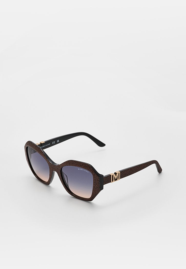 Braune, strukturierte Cat-Eye-Sonnenbrille mit Verlaufsgläsern und goldenem „M“-Logo am Bügel, liegend auf einer weißen Oberfläche.