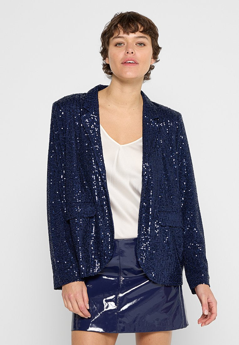 Navy-Blazer mit Pailletten, einem Reverskragen, zwei Fronttaschen und langen Ärmeln, getragen über einer hellen Satinbluse und einem glänzenden Minirock.