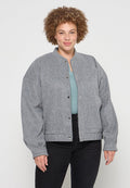 Grau, strukturierte Jacke mit rundem Halsausschnitt, Druckknöpfen und überschnittenen Schultern, getragen über einem hellblauen Oberteil und schwarzen Hosen.