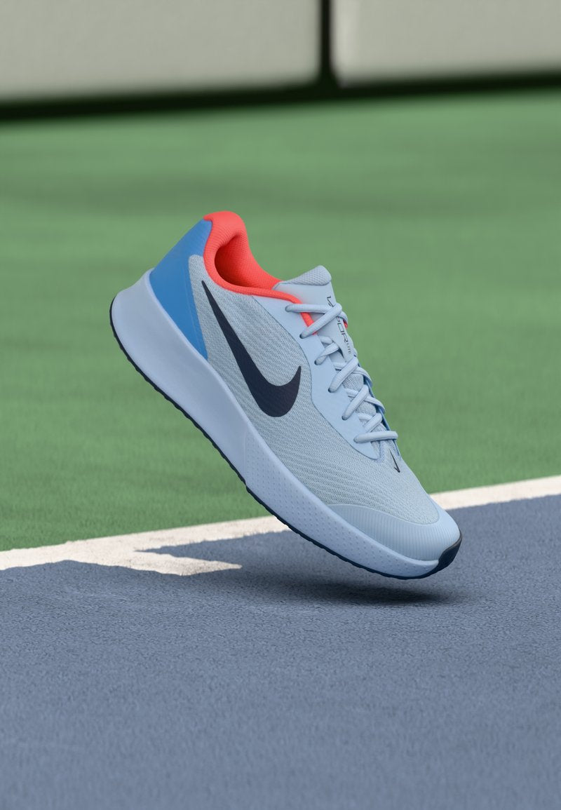 Hellblauer Sportschuh mit einem atmungsaktiven Mesh-Obermaterial, dunkelblauer Sohle und lebendigen korallenfarbenen Akzenten. Hat ein geschwungenes Design und eine Schnürung.