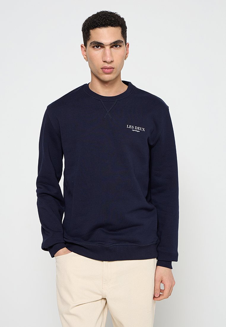 Marineblaue Sweatshirt aus weichem Baumwollmaterial, mit Rundhalsausschnitt, langen Ärmeln und gesticktem 'LES DEUX'-Logo auf der Brust.