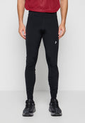 Mann trägt schwarze eng anliegende Sporthose mit Seitentasche, rotes strukturiertes Shirt und schwarze Laufschuhe, steht vor einfachem Hintergrund.