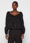 Schwarze Peplum-Bluse mit gepufften Ärmeln, strukturierten Fransen an dem Saum und einem V-Ausschnitt, aus glattem Stoff gefertigt. Kombiniert mit gestreiften Hosen.