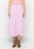 Frau in einem gerippten lavendelfarbenen Midiskirt, rosa figurbetontem ärmellosem Oberteil und braunen Wildleder-Ankle-Boots mit Schnallen.