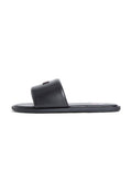 Schwarze Slide-Sandale mit einem Riemen, flacher Sohle und kleinem metallischem rechteckigem Logo auf dem Riemen, seitliche Ansicht auf weißem Hintergrund.
