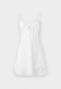 Weißes ärmelloses Sommerkleid mit dünnen Spitzenriemen und einer Schleifendetail vorne vor einfachem Hintergrund.