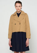 Beige Trenchcoat mit großen Revers, doppelreihigen Knöpfen und Seitentaschen, getragen über einem marineblauen Kleid. Glatte Textur.