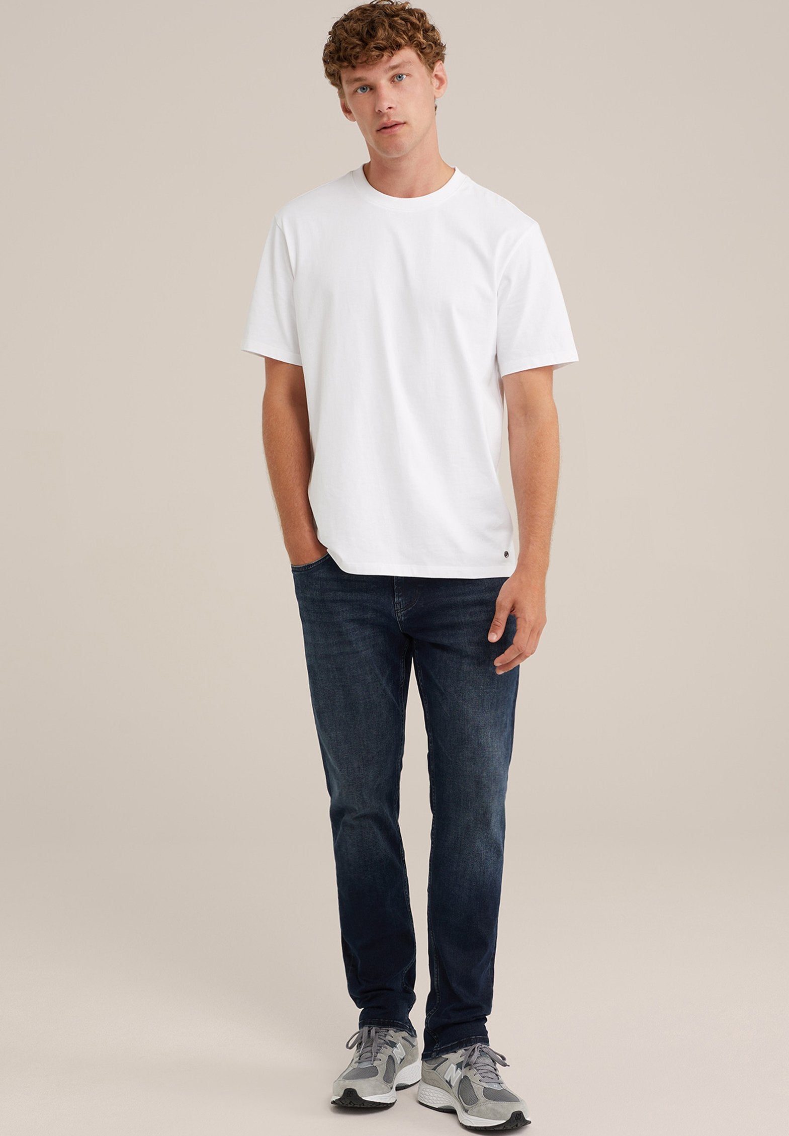 Weißes Baumwoll-T-Shirt mit rundem Ausschnitt, kombiniert mit dunkelblauen Jeans und grauen Sportschuhen mit dunkleren Akzenten.
