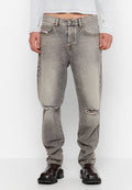 Person trägt ausgebleichte graue zerrissene Jeans mit Löchern an beiden Knien, ein weißes, geripptes Langarmoberteil und schwarze Lederstiefel.