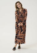 Langärmliges, marineblaues Kleid mit orangefarbenen Blätternmuster. Leichter Stoff, geraffter Oberteil und knöchellang. Kombiniert mit schwarzen Plateausandalen.