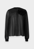 Schwarze Bluse mit langen transparenten Ärmeln, die vordere Falten und ein mehrlagiges Stoffblütenakzent an der linken Schulter aufweist. Knopfverschluss am Hals.