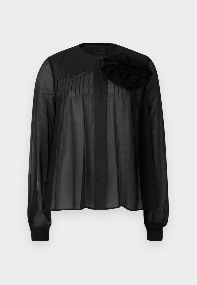 Schwarze Bluse mit langen transparenten Ärmeln, die vordere Falten und ein mehrlagiges Stoffblütenakzent an der linken Schulter aufweist. Knopfverschluss am Hals.