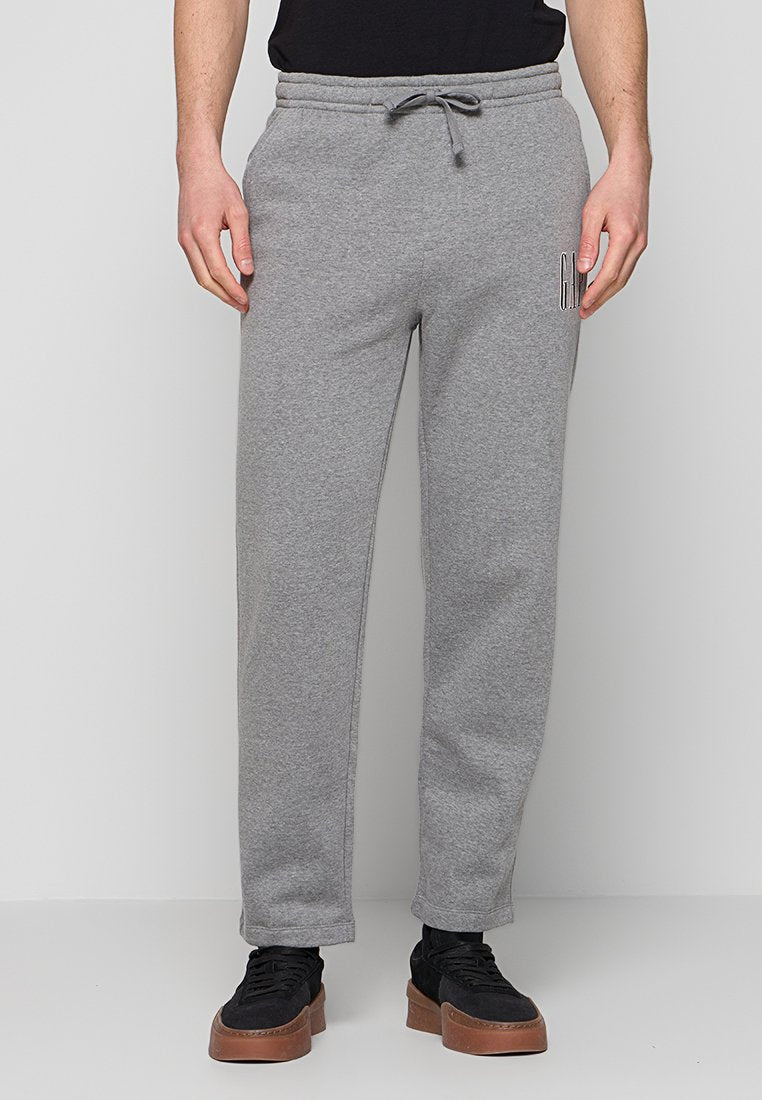 Mann trägt hellgraue Jogginghose mit Seitentaschen und Kordelzug, kombiniert mit schwarzen Sneakers mit braunen Sohlen.