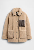 Beige Fleecejacke mit strukturierter Oberfläche, ausgestattet mit einer braunen Leder-Reißverschlusstasche und zwei großen Vordertaschen, rundem Kragen und Knopfverschluss.