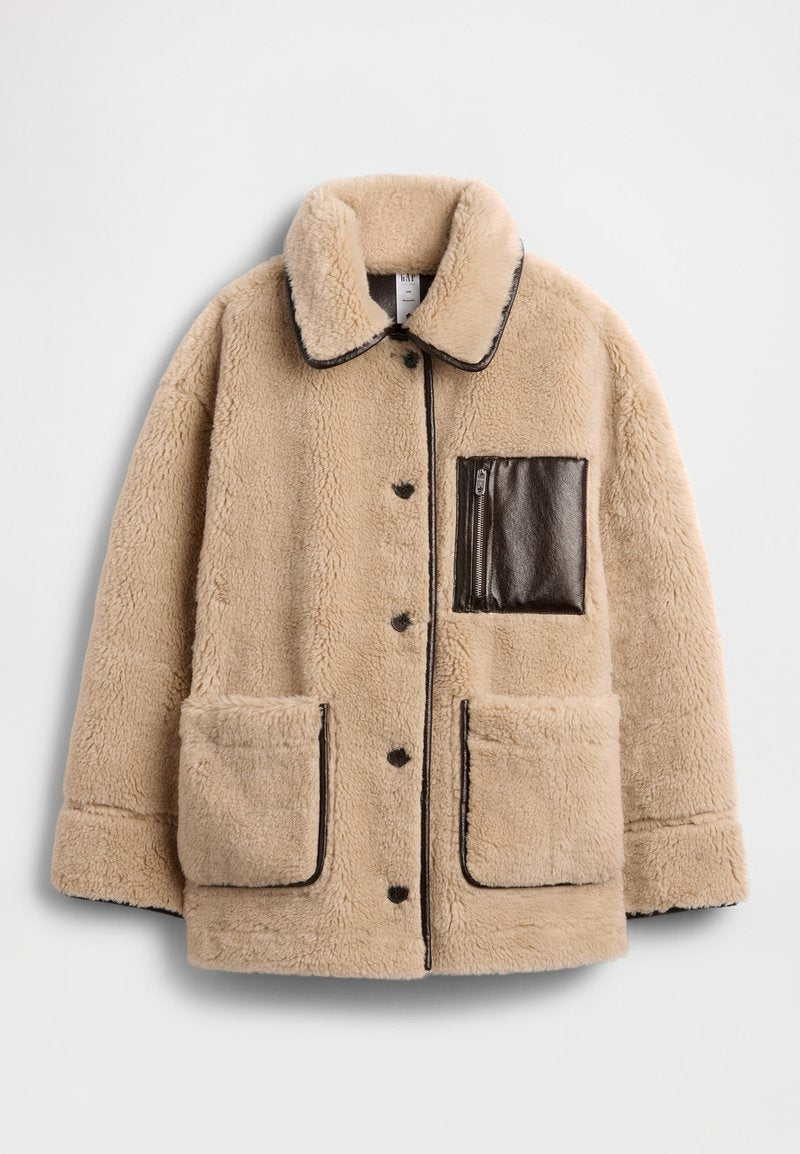 Beige Fleecejacke mit strukturierter Oberfläche, ausgestattet mit einer braunen Leder-Reißverschlusstasche und zwei großen Vordertaschen, rundem Kragen und Knopfverschluss.