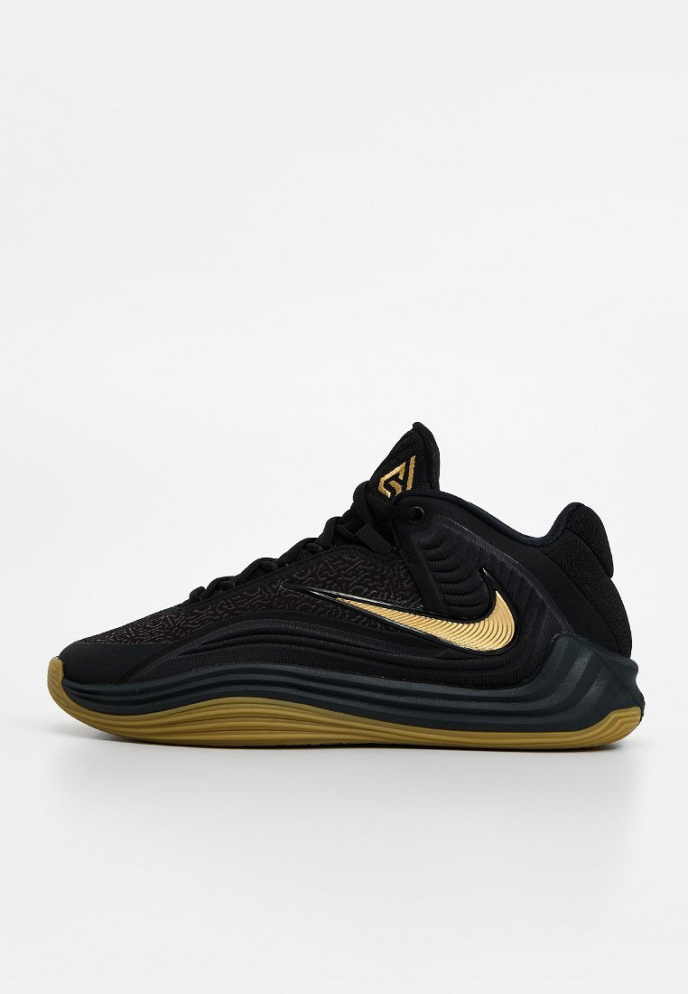 Schwarzer und goldener Nike-Sneaker mit niedrigem Schnitt, strukturiertem Obermaterial, goldenem Swoosh-Logo und welliger schwarzer und goldener Sohle, Seitenansicht vor weißem Hintergrund.