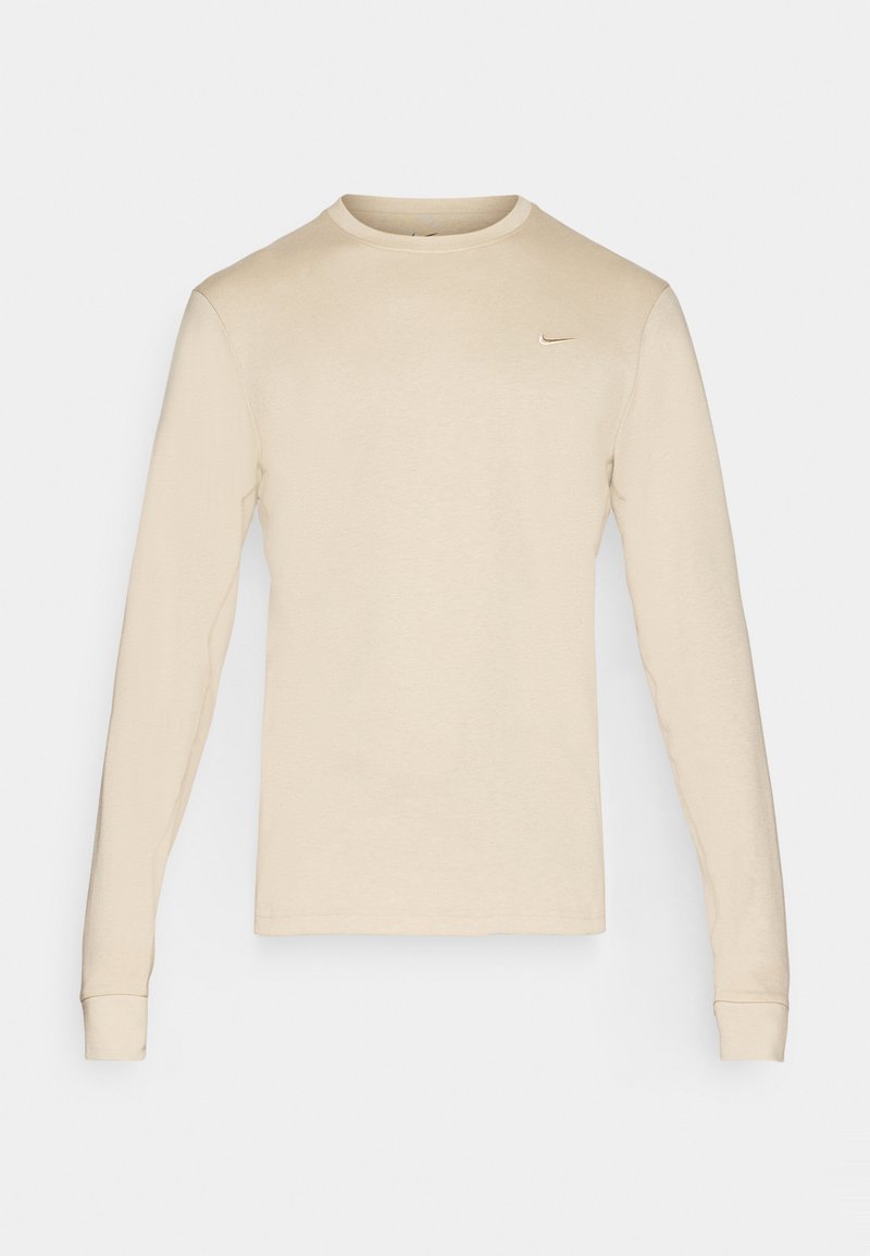 Beige Langarm-Nike-T-Shirt mit rundem Ausschnitt und kleinem Logo auf der oberen linken Seite. Glattes Material mit enganliegenden Bündchen.
