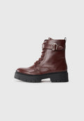 Braune Leder-Stiefeletten mit einer dicken, schwarzen Gummisohle, Schnürvorderseite und einem Riemen mit einer silbernen Schnalle als Akzent. Glatte Oberfläche.